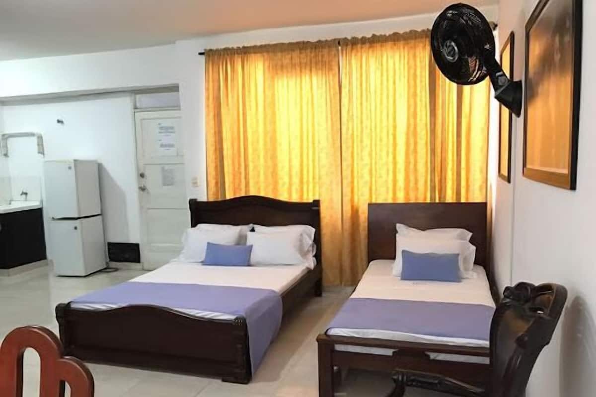 A hotel room with two beds, a desk, a chair, a refrigerator, and a window with curtains.