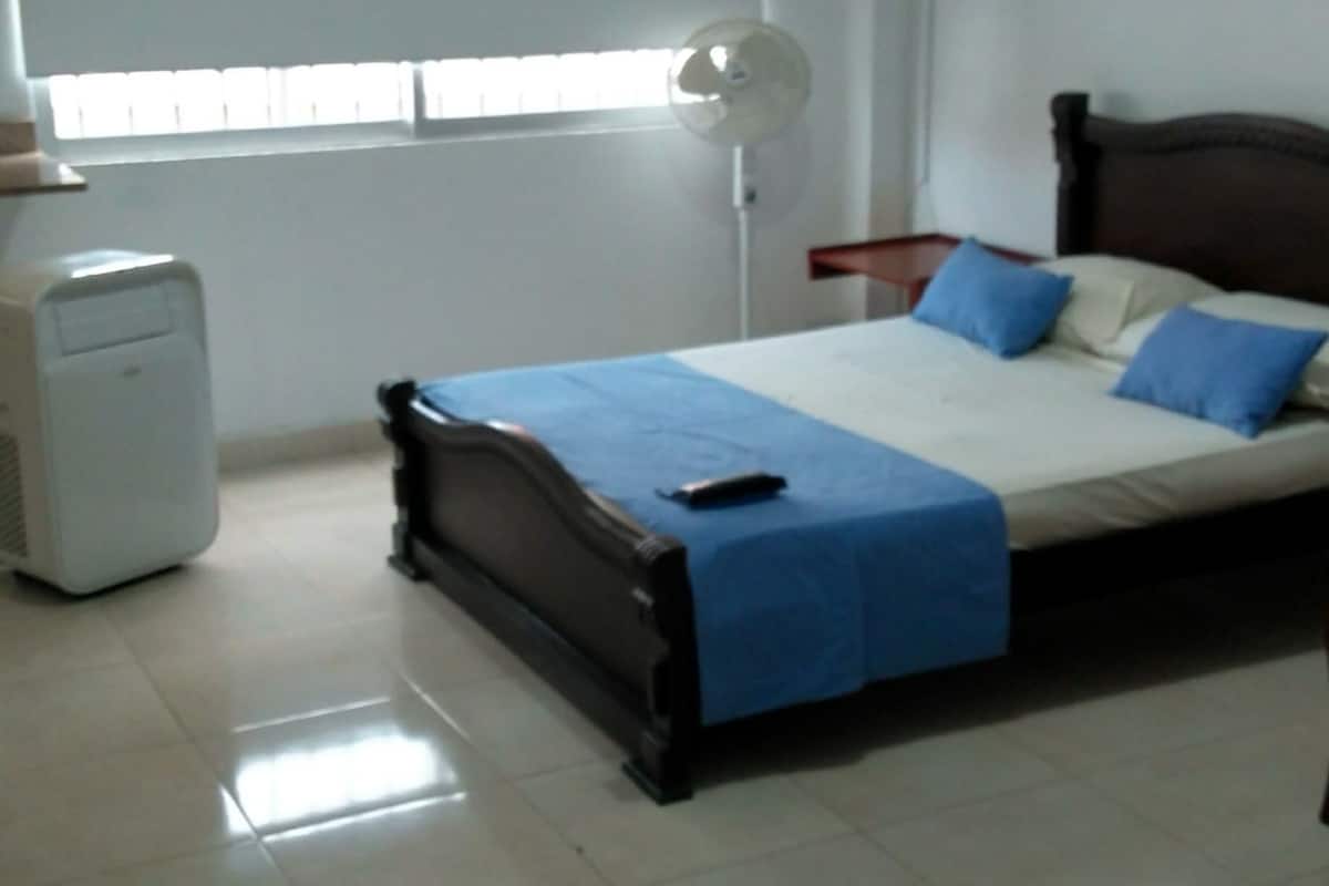 A bedroom with a bed, a bedside table, a lamp, and a window.