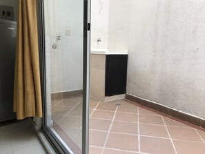 A room with a sliding glass door, a tiled floor, a small kitchenette, and a white wall. - ARCO Apartasuites (Cali)