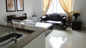 A hotel room with a bed, a chair, a desk, a sink, and a window with curtains. - ARCO Apartasuites (Cali)