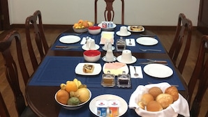 Una mesa de comedor dispuesta con platos, tazones y diferentes alimentos, rodeada de sillas de madera.