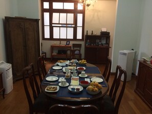 A dining room with a round table set for a meal, surrounded by wooden chairs. There is a window with frosted glass panes, a chandelier, and a small side table with a lamp. - Larq'a Park Rooms (Lima)