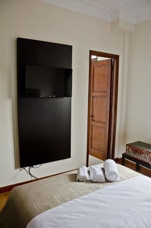 A hotel room with a large bed, a flat-screen TV mounted on the wall, a wooden door, and a small table with a decorative item. - Larq'a Park Rooms (Lima)
