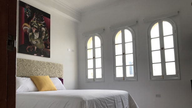 Un dormitorio con una cama, un ventanal grande y un cuadro en la pared.
