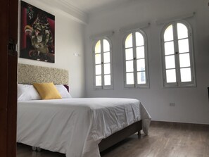 A bedroom with a bed, a large window, and a painting on the wall. - Larq'a Park Rooms (Lima)