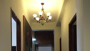 Un pasillo con suelo de madera, un candelabro, cuadros en las paredes y una puerta a la izquierda.