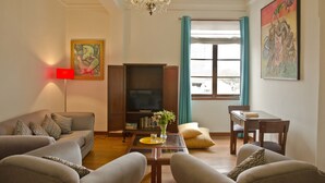 Una sala de estar con sofá, sillones, una mesa de centro, televisor, estantería y un cuadro.