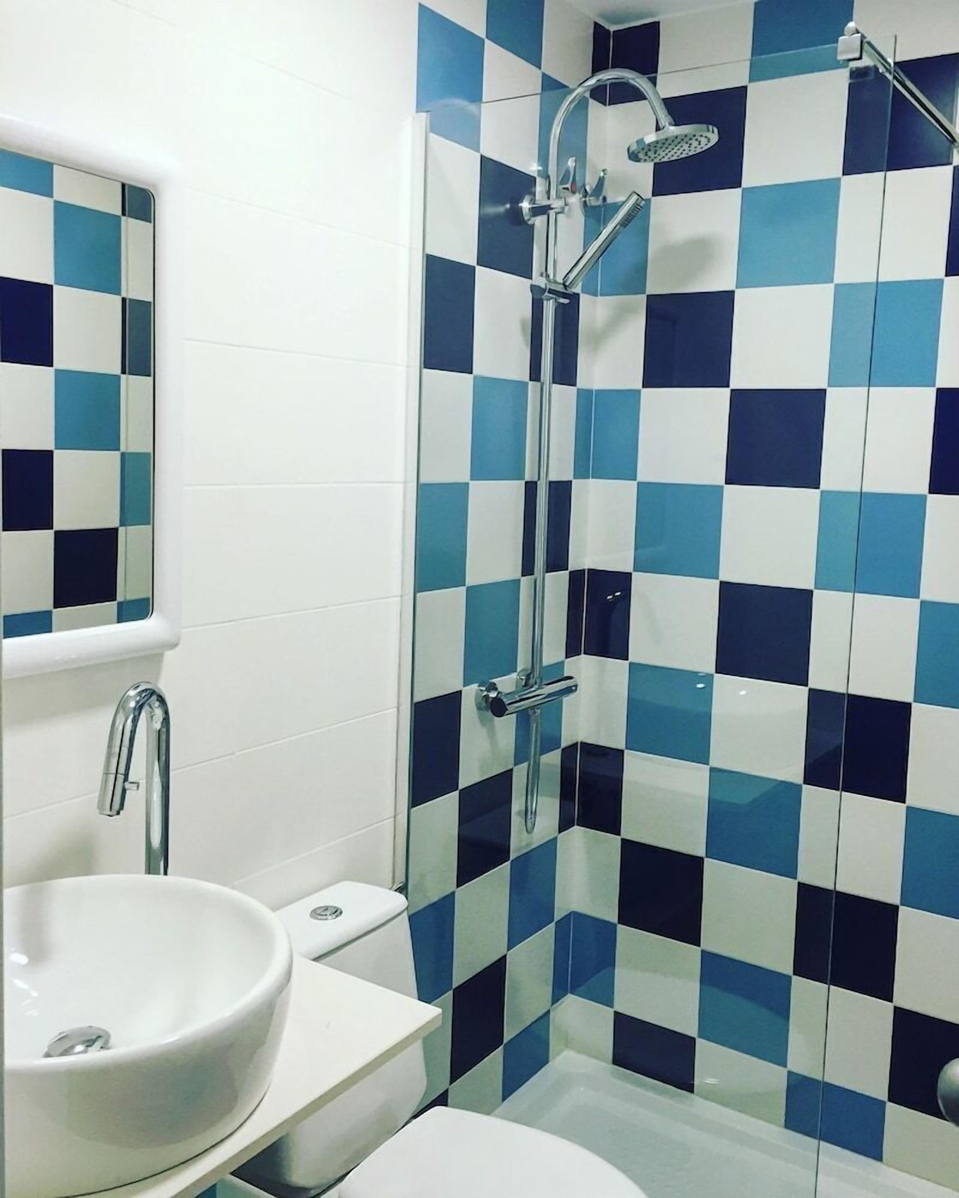 Un baño con suelo de baldosas de estampado de cuadros, un lavabo blanco, un inodoro y una ducha con cabezal de mano.
