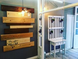 Quarto com prateleira de madeira fixada na parede, com mãos impressas, e um banco branco com plantas em vasos.
