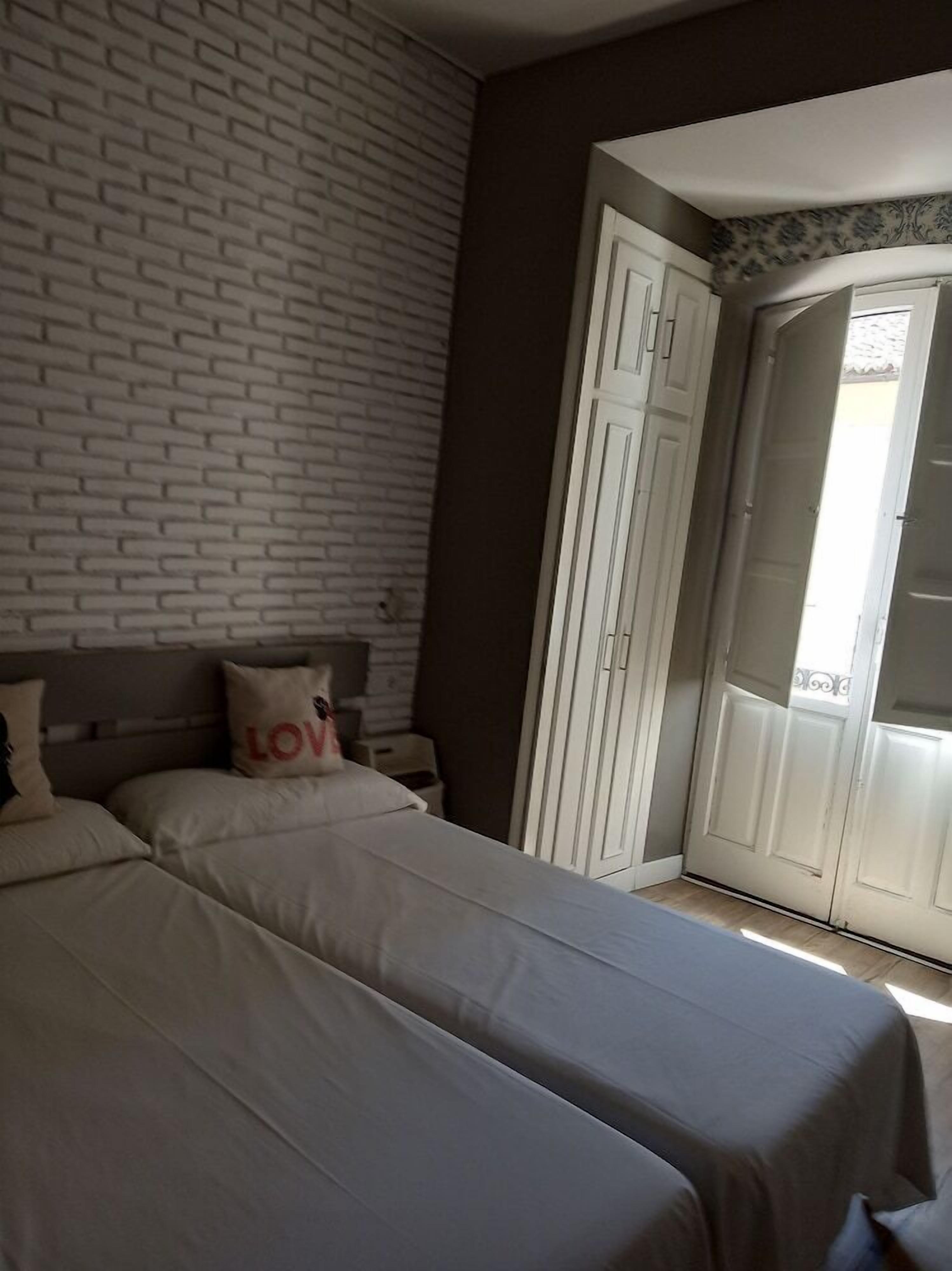 Un dormitorio con dos camas, pared con diseño de ladrillo, puerta blanca y vista al exterior.