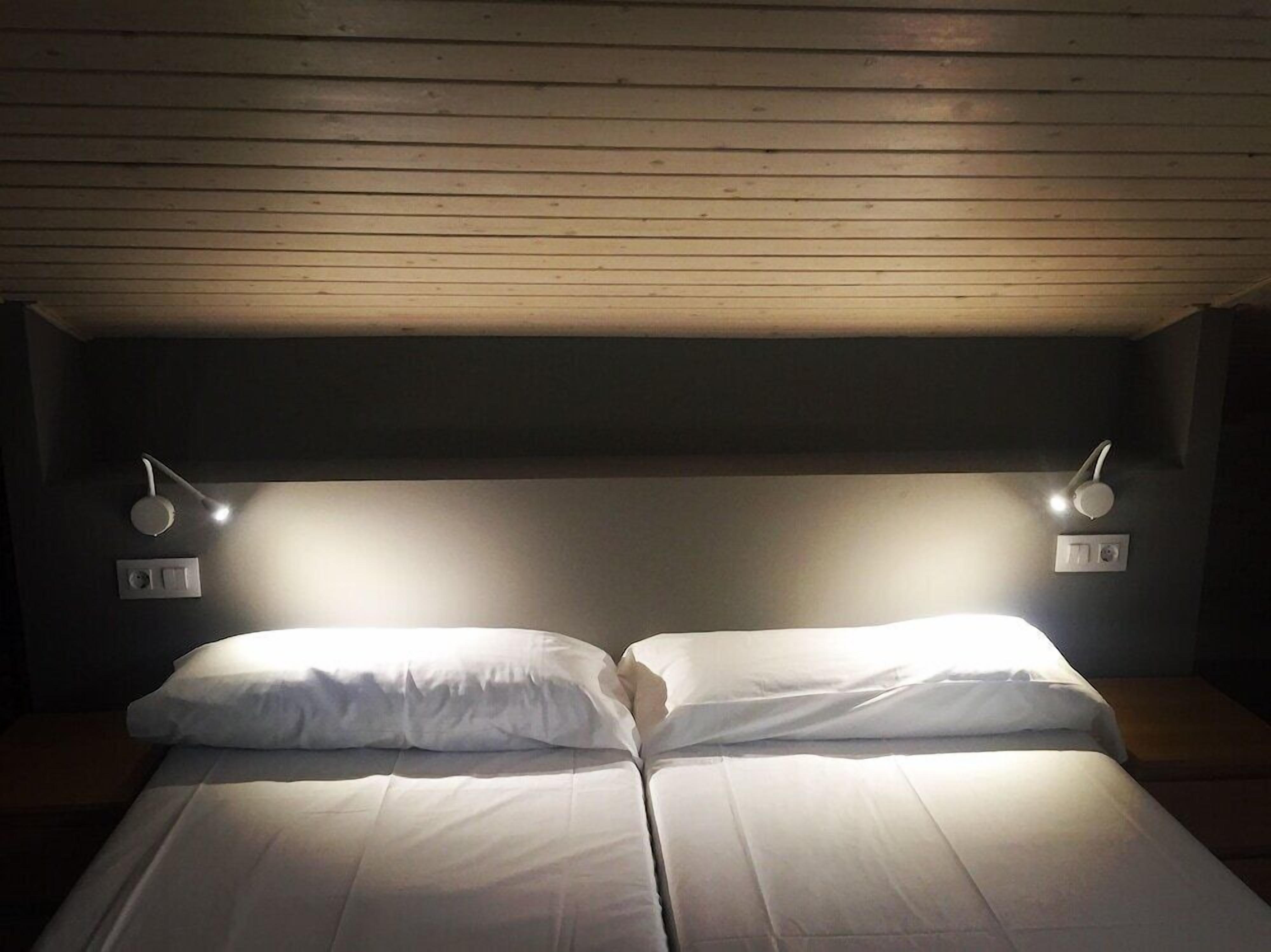 Una habitación con una cama, dos lámparas de noche y techo de madera.