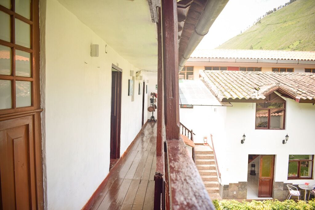 A corridor with wooden railings, white walls, and a view of a building with a tiled roof and a staircase.