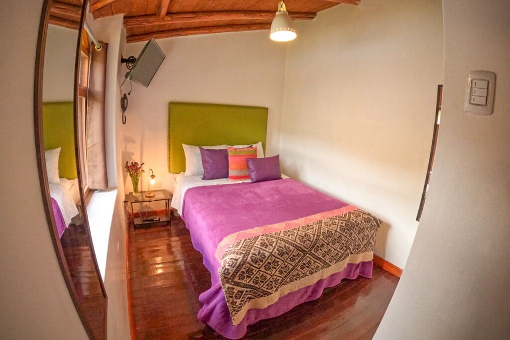 A bedroom with a bed, a bedside table with a lamp, and a mirror.