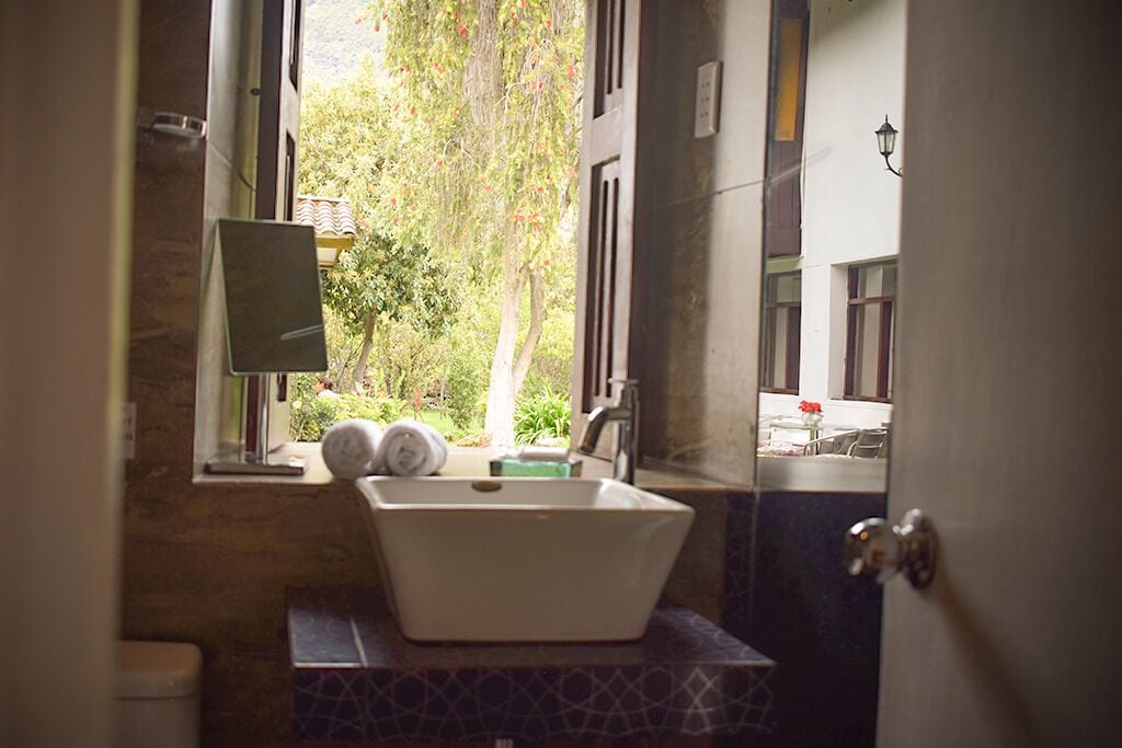 Un baño con lavamanos blanco, un espejo y ventana con vistas a un jardín.