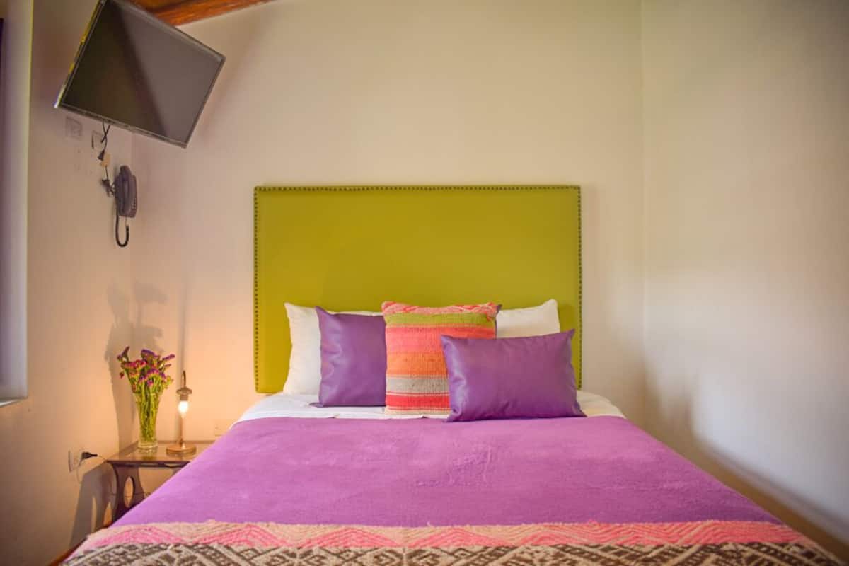 A bedroom with a green headboard, purple bedding, and a patterned rug.