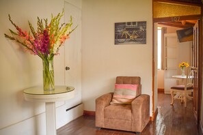 A room with a glass table holding a vase of flowers, a brown armchair with a striped pillow, and a bicycle painting on the wall. - RHOUSE Calca (Calca)