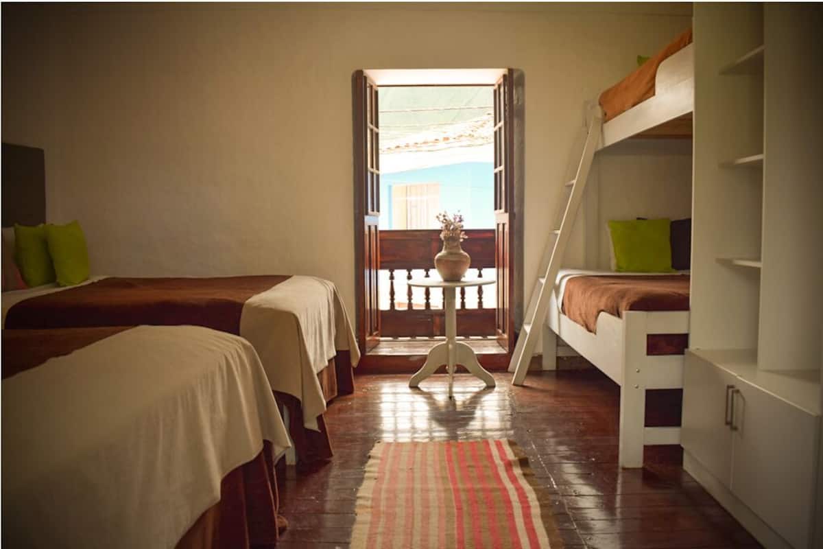 A room with two beds, a small table, and a balcony with a railing.