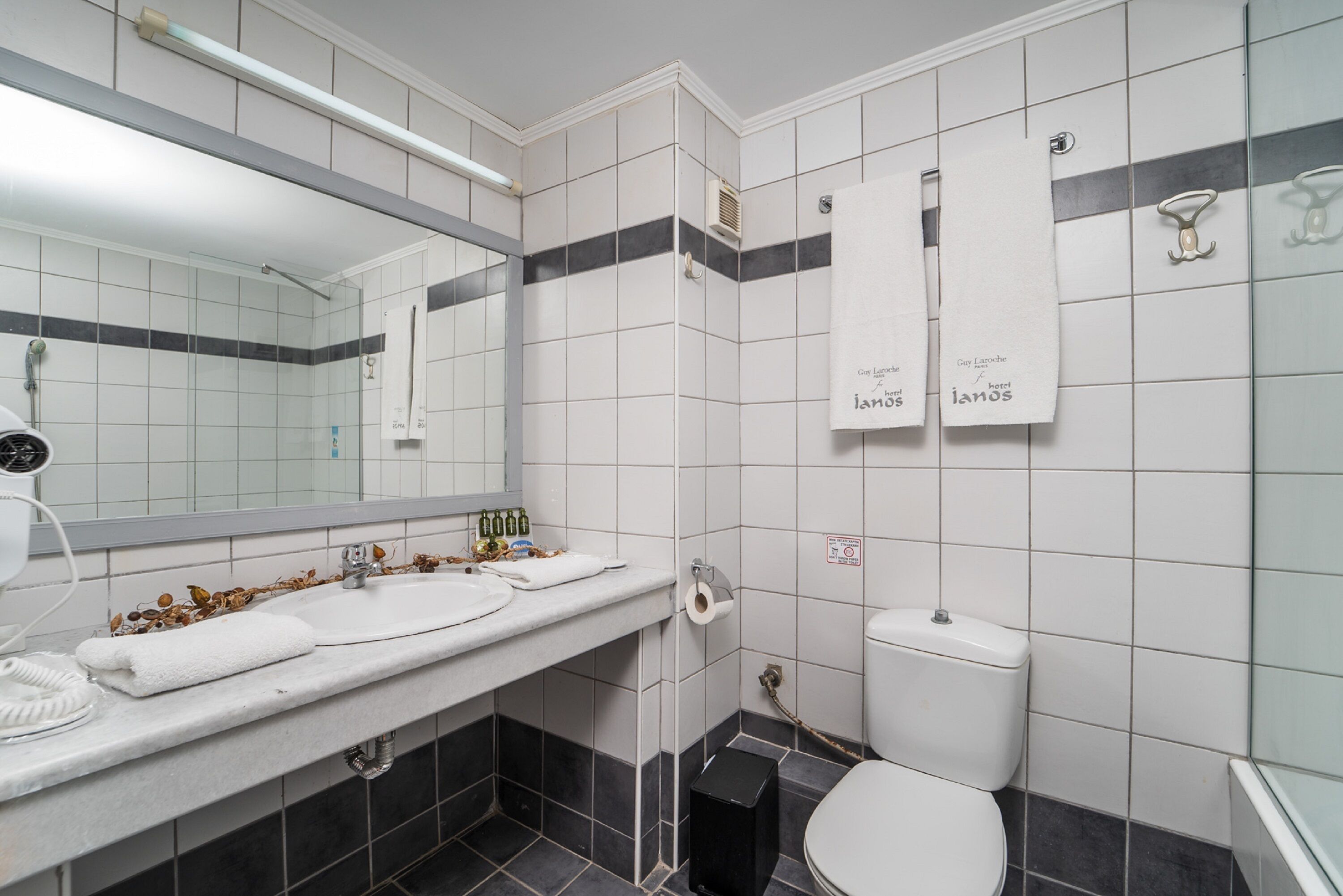 A bathroom with a white sink, mirror, and toilet. There are towels hanging on the wall and a showerhead above the sink.