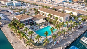 Un resort con piscina rodeada de palmeras, un puerto deportivo y un estacionamiento.