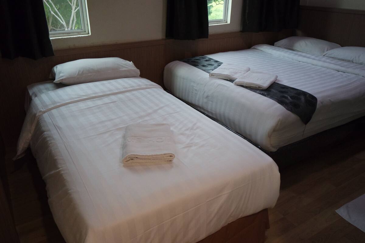 Two single beds with white linens and towels, a window with curtains, and a wooden floor.
