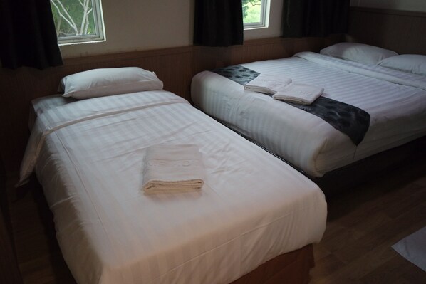 Two single beds with white linens and towels, a window with curtains, and a wooden floor. - Home Hotel Labuan (Labuan)