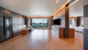 A modern hotel room with a wooden floor, a sofa, a dining area, a TV, and a balcony with a city view. - Incheon STAY Hotel (Incheon)