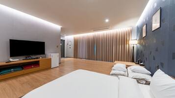 A modern hotel room with a large bed, a flat-screen TV, wooden flooring, and a sliding door leading to a bathroom.