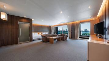 A modern hotel room with a large bed, a seating area with a coffee table, a TV, and a city view through the window.