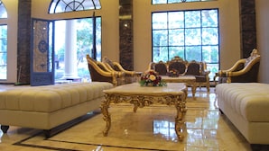 Um hall de entrada luxuoso com móveis elaborados, grandes janelas e piso de mármore.