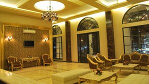 Um hall de entrada luxuoso com móveis elaborados, um candelabro e amplas janelas em arco.