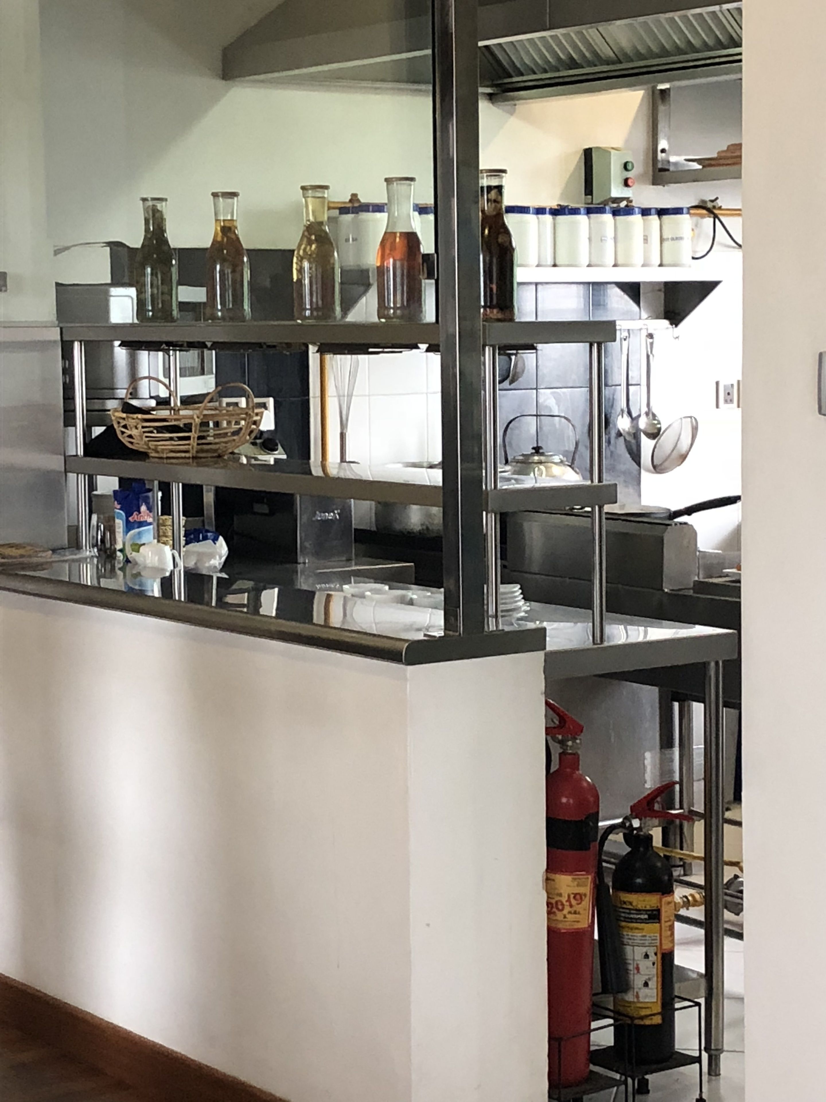 A kitchen area with stainless steel appliances, a fire extinguisher, and shelves with glass containers.