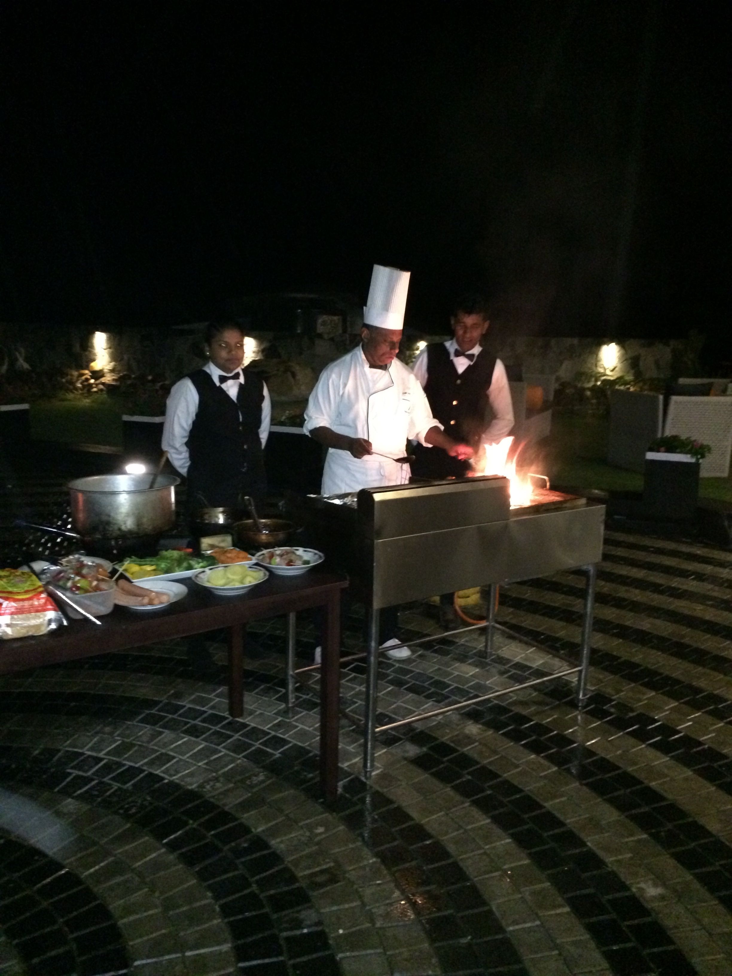 A chef cooking outdoors at night with a table of food in front of him.