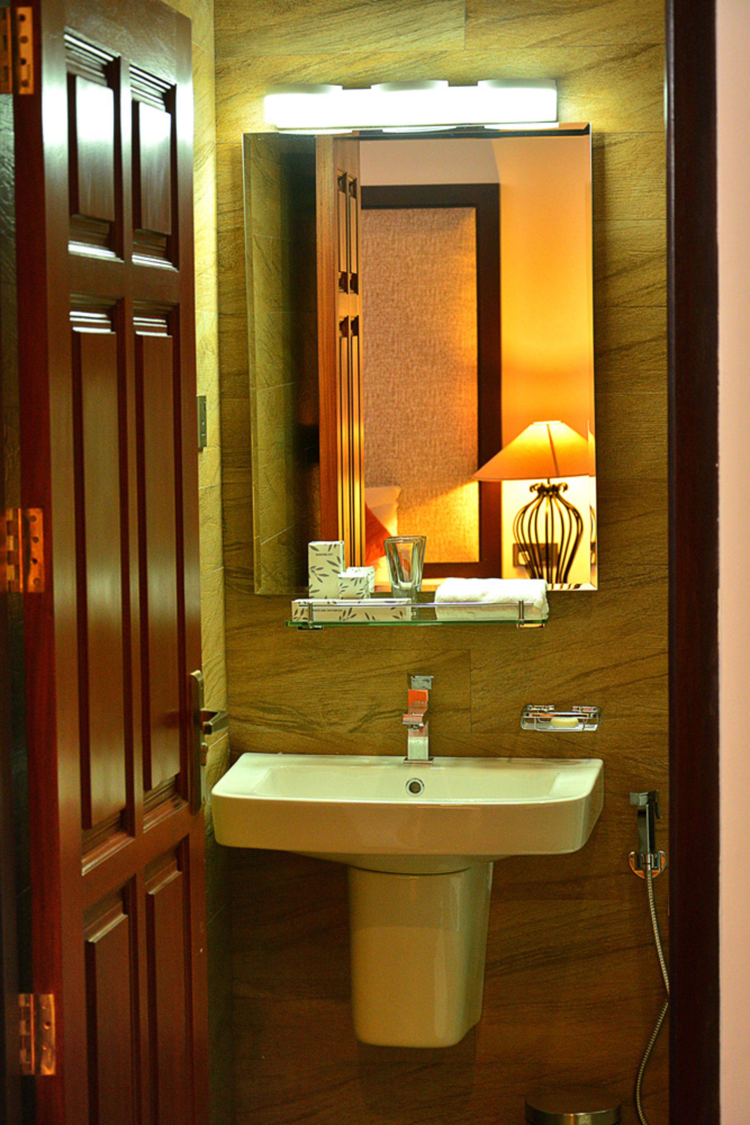 Une salle de bain avec un meuble-lavabo en bois, un évier, un miroir et une lampe fixée au mur.
