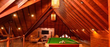 Habitación en el ático con mesa de billar, vigas de madera y televisor.