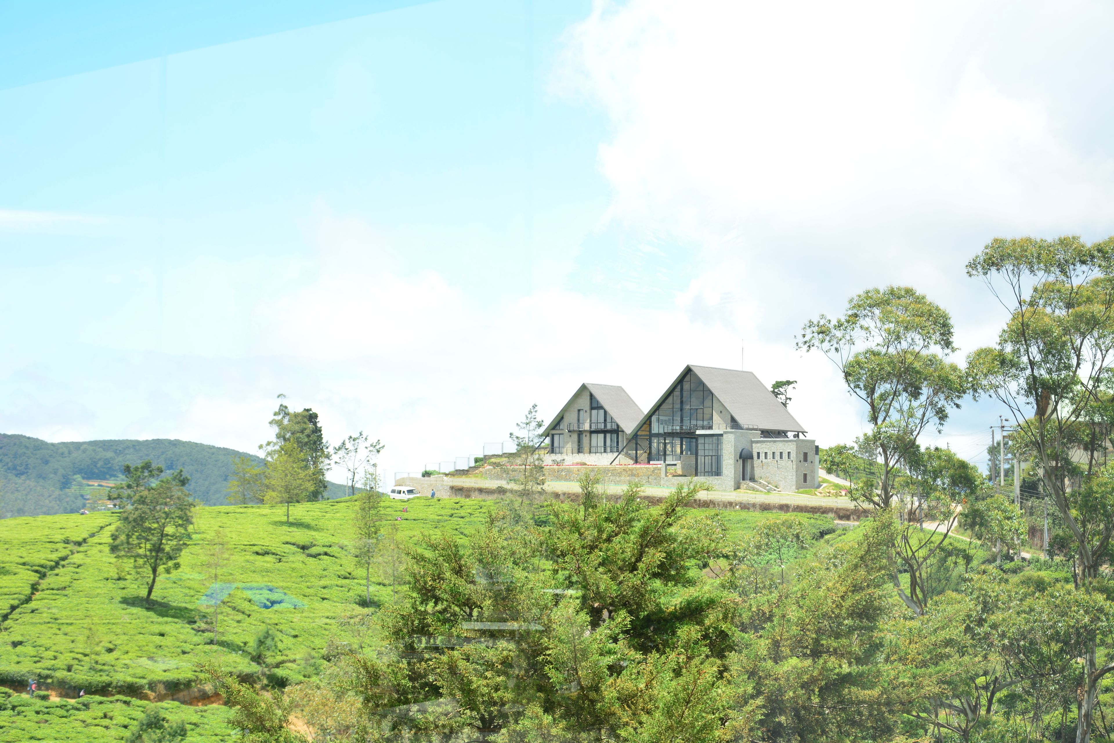 A modern house with a large glass facade, situated on a green hill with a clear sky.