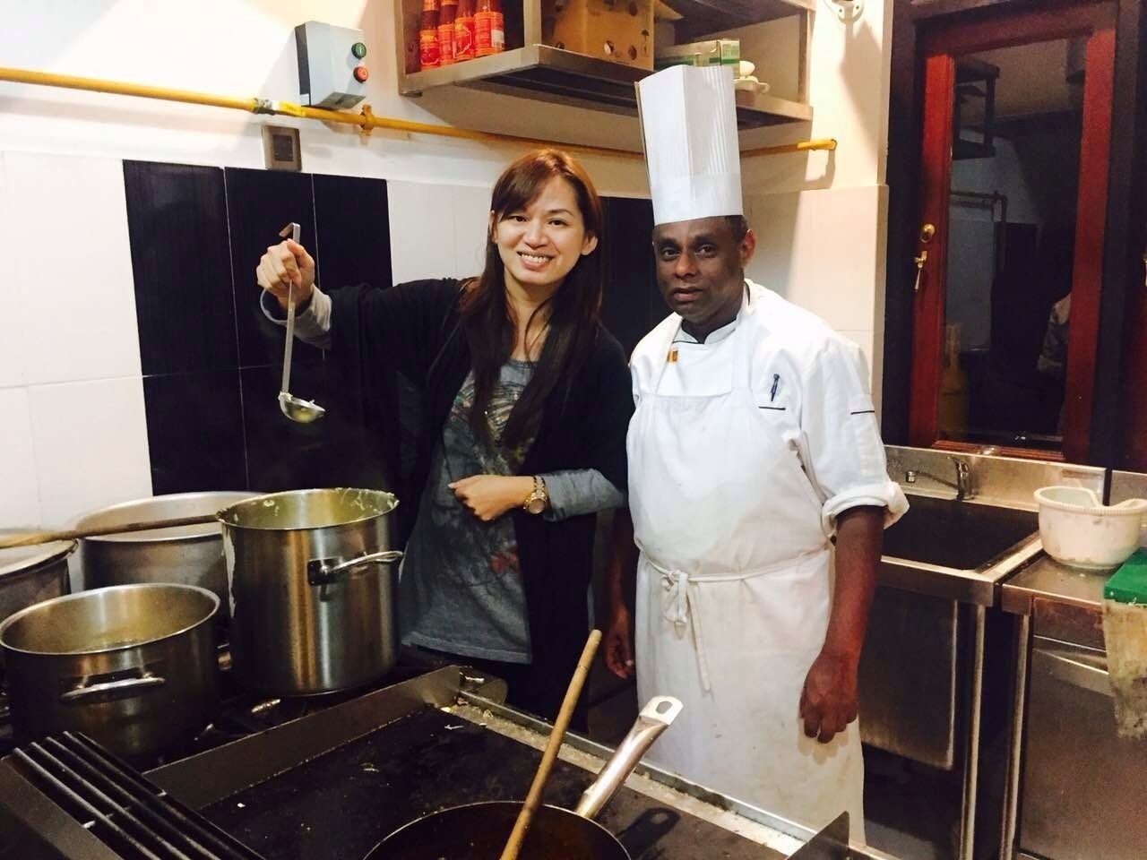 A kitchen with stainless steel pots and pans, a stove, and a chef's hat on a person.