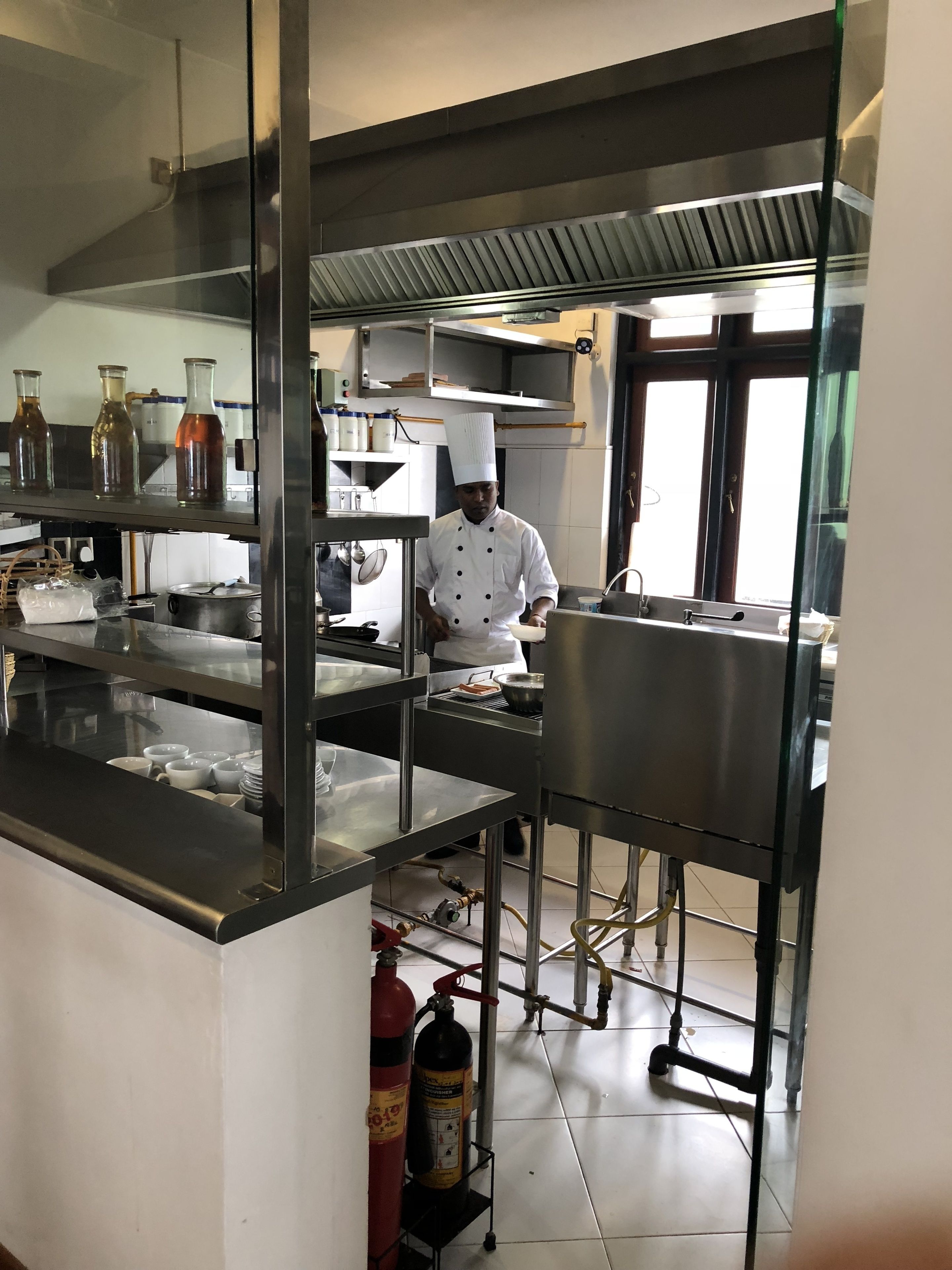 A commercial kitchen with stainless steel appliances, a chef in uniform, and a fire extinguisher on the floor.