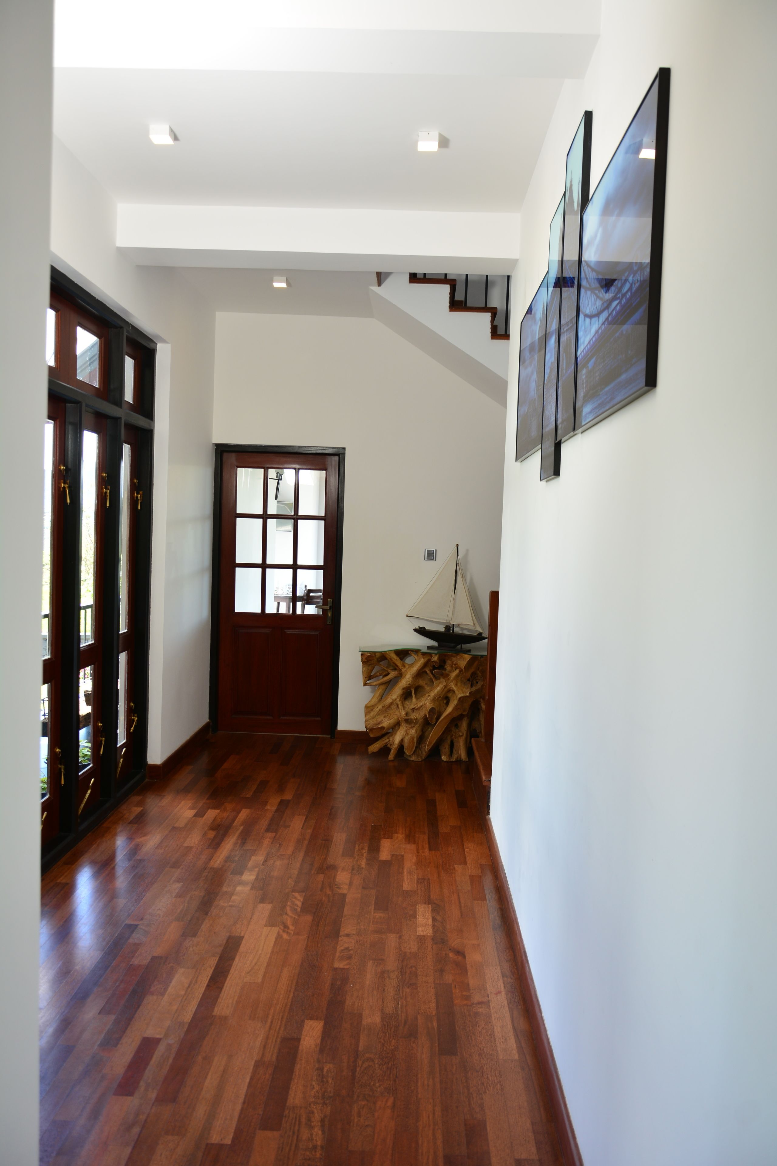 A hallway with wooden flooring, a wooden door with glass panels, and a staircase leading to an upper level.