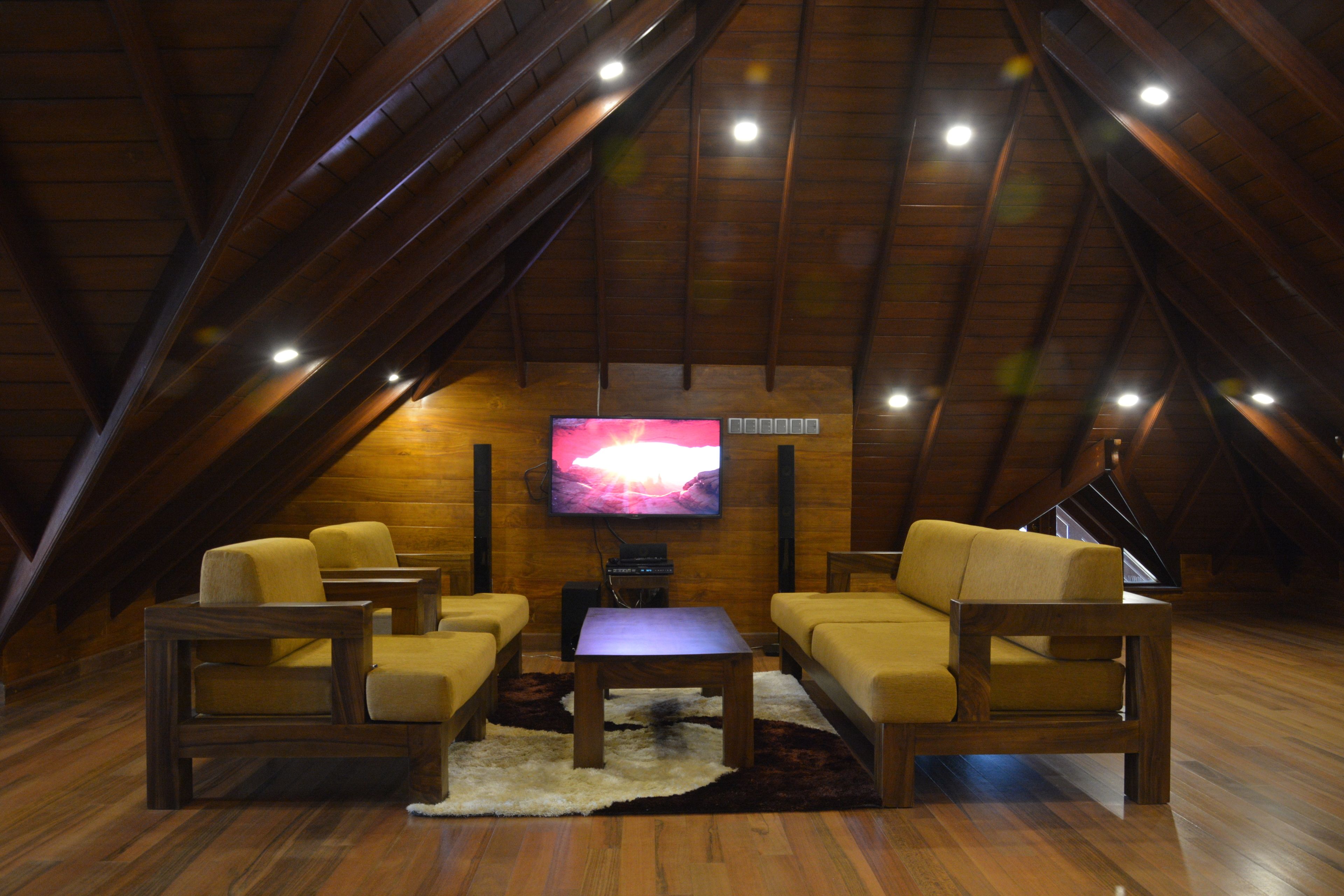 An attic room with wooden beams, a flat-screen TV, and two sofas.