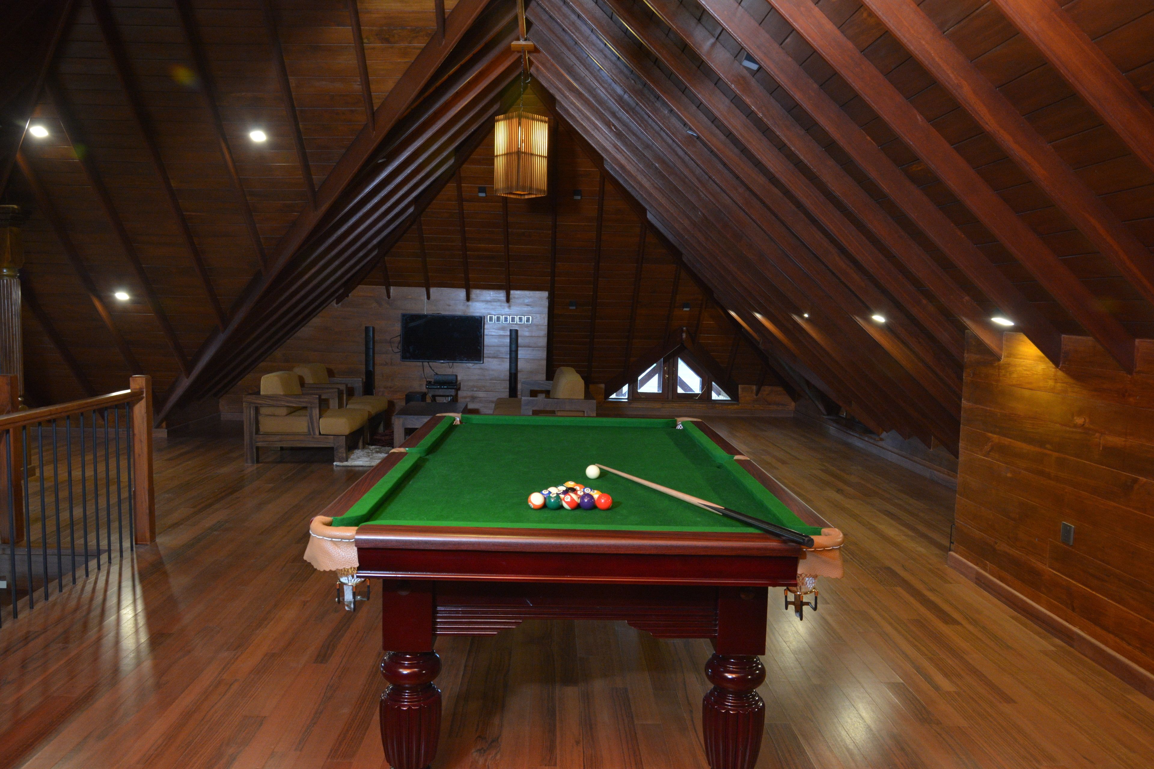 A pool table in a room with wooden beams and a staircase.