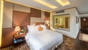 Habitación de hotel con una cama grande, una mesita de noche con lámpara, un espejo y una estantería.