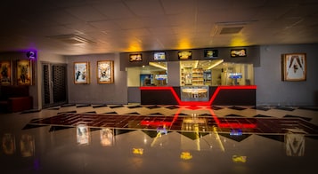 Un vestíbulo de cine con piso a cuadros, letreros de neón y una barra de venta de aperitivos.