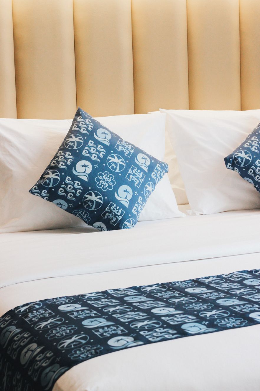 Un lit avec une tête de lit beige, des oreillers blancs et une couvre-lit bleue à motifs.