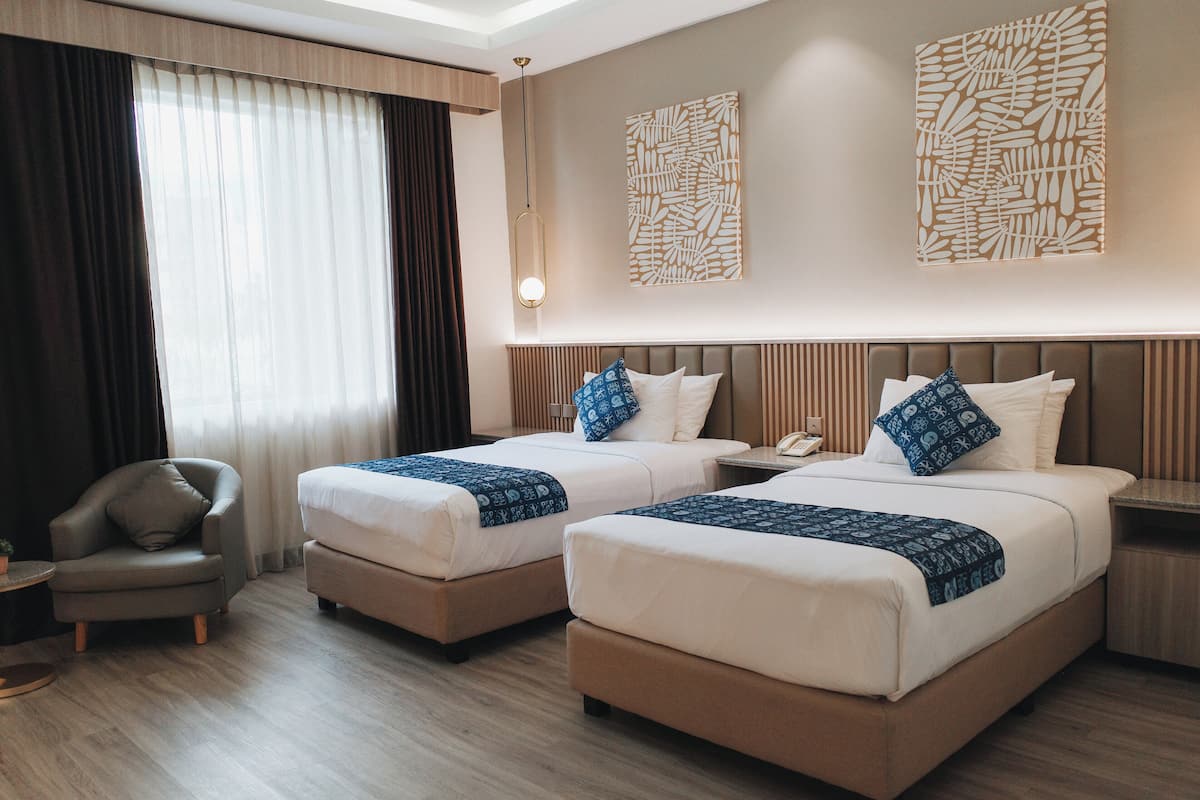 A hotel room with two beds, a chair, a bedside table, and a wall-mounted artwork.