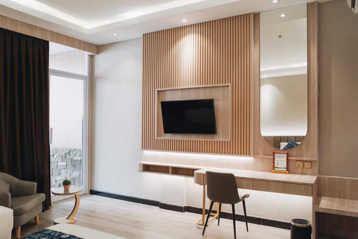 A modern living room with a flat-screen TV mounted on a wooden panel wall, a seating area with a sofa and a chair, and a small side table with a plant.
