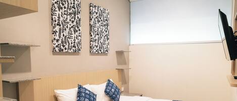A hotel room with a bed, a telephone, a TV, and two wall-mounted artwork pieces.