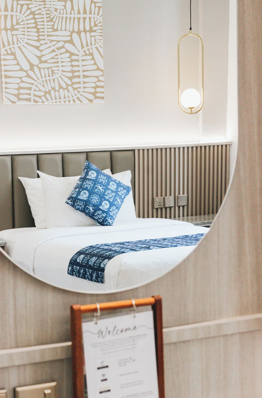 Habitación de hotel moderna con un espejo grande que refleja la cama y una lámpara fijada a la pared.