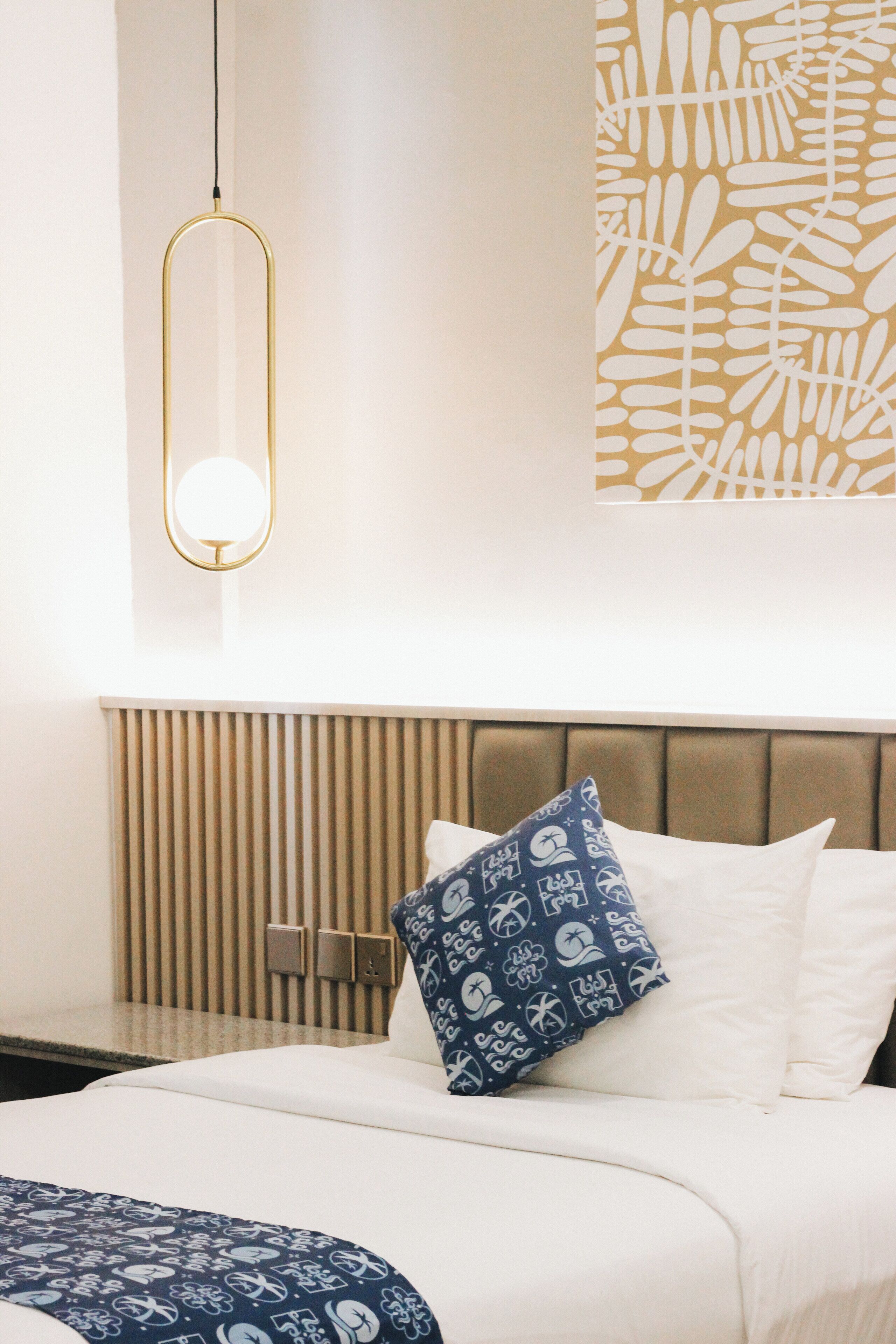 Habitación de hotel con cama, mesita de noche, lámpara de pared y un panel decorativo en la pared.