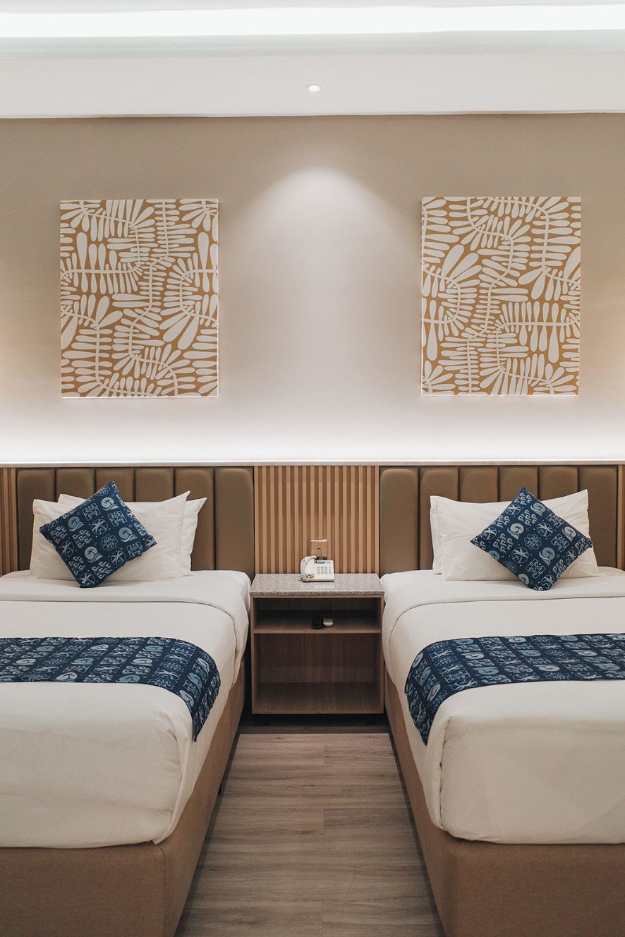 A hotel room with two beds, a nightstand, and two wall-mounted abstract art pieces.