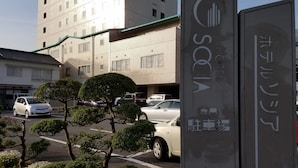 Señal de hotel con diseño moderno y un estacionamiento con coches y árboles bien cuidados.